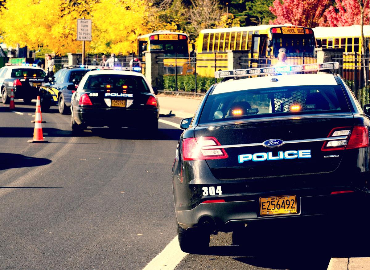 police cars are lined up in a row on the street next to school buses