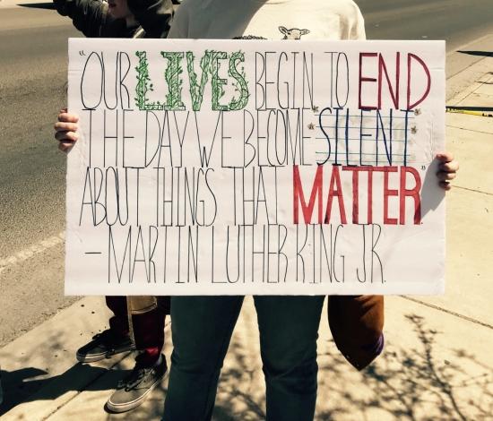 A person holding a sign that says, "Our lives begin to end the day we become silent about things that matter - Martin Luther King Jr".